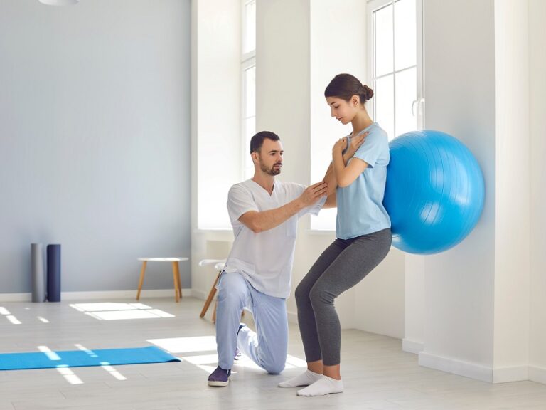 Physiotherapist helping young woman recover from back injury using big soft ball